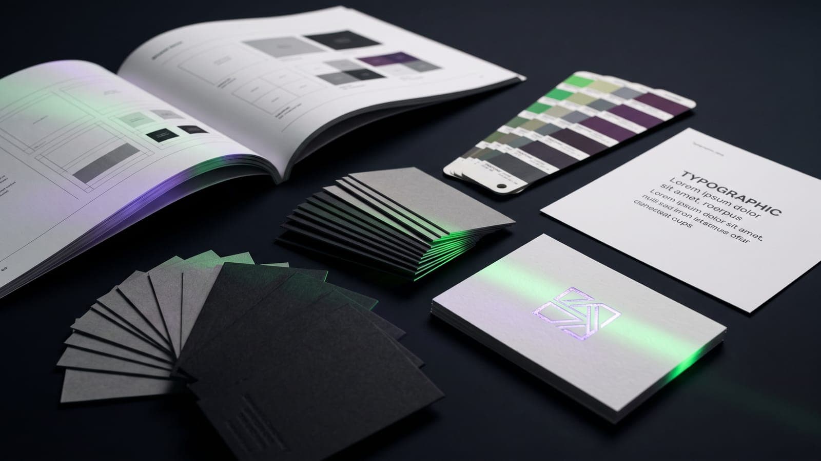 Manual de marca abierto rodeado de abanico Pantone, espécimen tipográfico y tarjetas en abanico, una con logo en foil violeta, bajo luz verde, al desglosar el costo de imagen corporativa en México