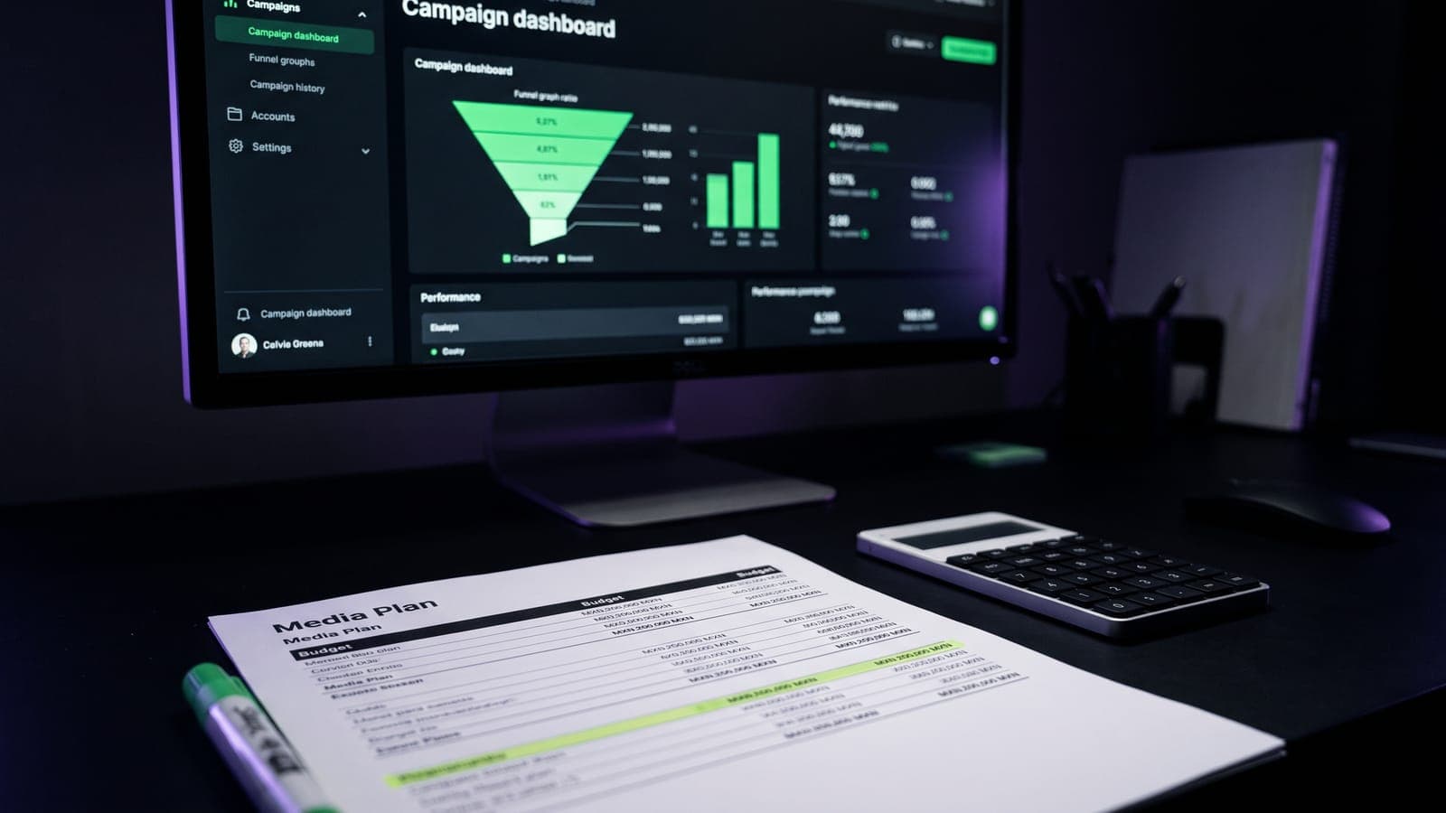 Monitor con dashboard de campañas con embudo y gráficas verdes junto a un media plan impreso con presupuesto en pesos y calculadora, en una agencia de marketing digital en CDMX