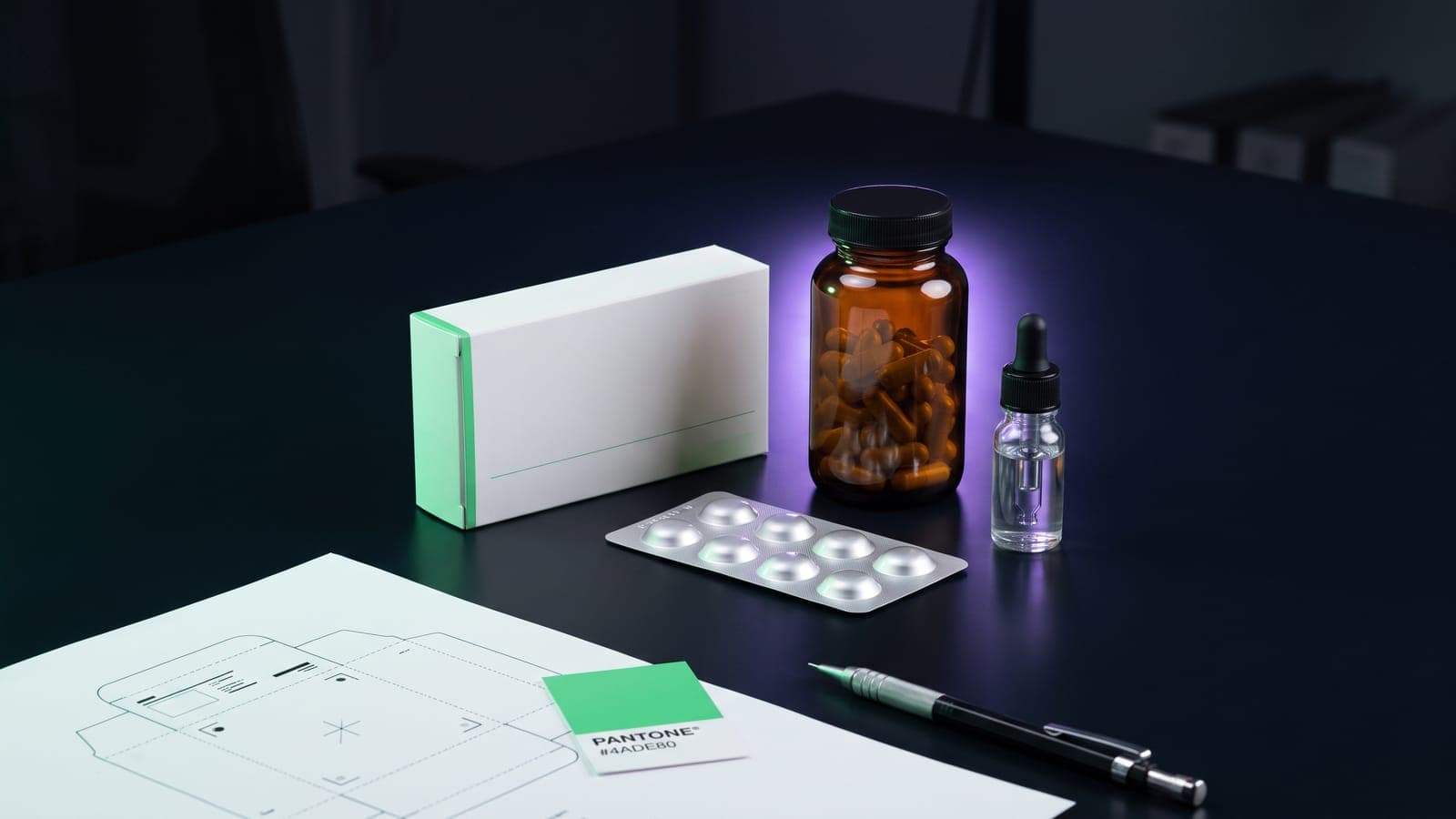 Caja de medicamento, frasco ámbar con cápsulas, blíster plateado y die-line troquelado sobre mesa oscura: packaging farmacéutico para registrar en la clase 5 de Niza