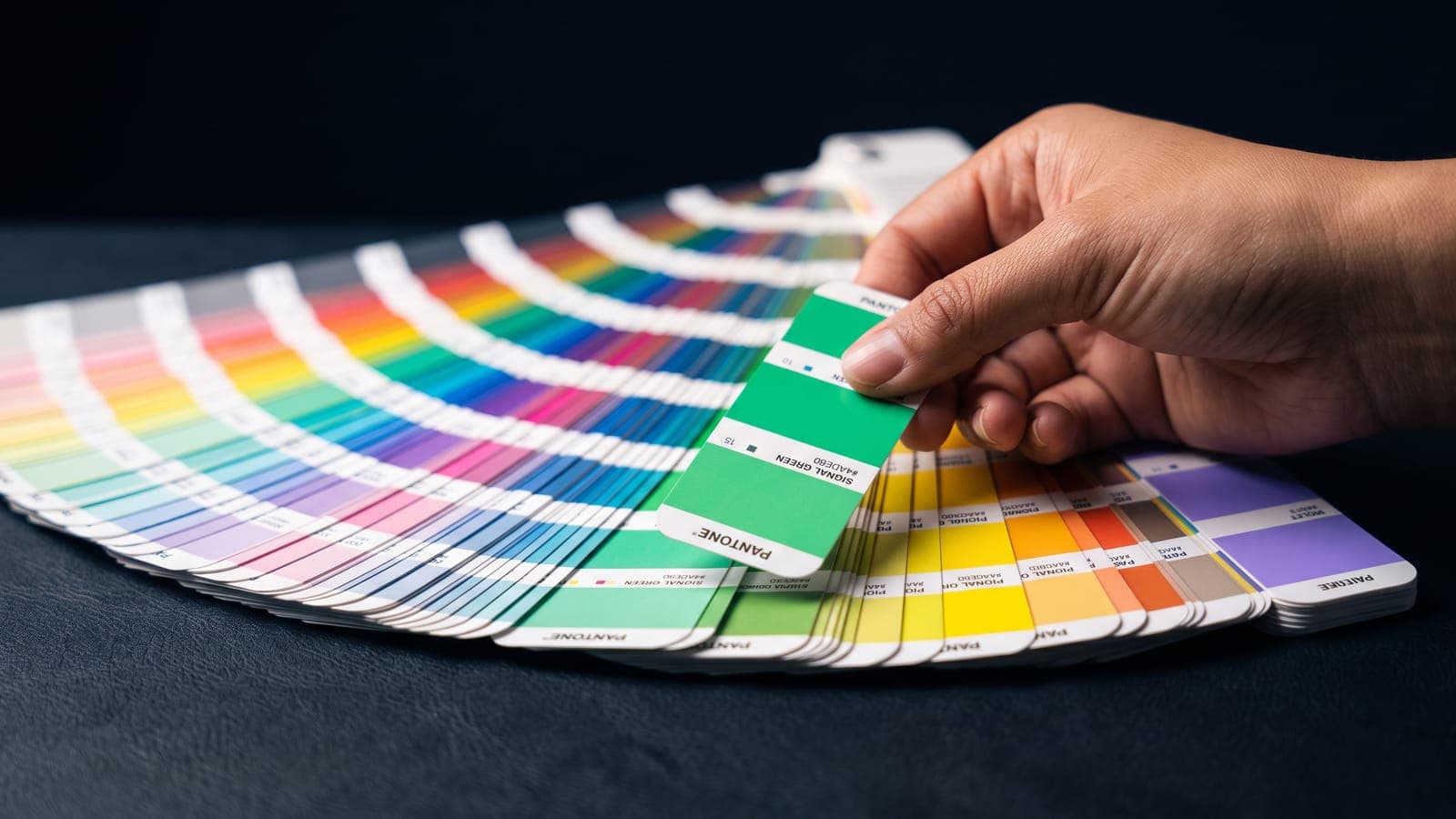 Mano eligiendo una muestra Pantone verde señal entre abanicos de colores desplegados, al definir los colores para un negocio