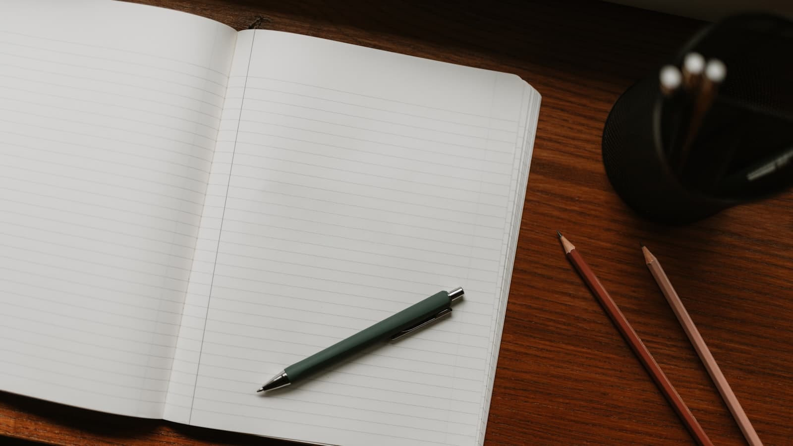 Cuaderno abierto con pluma y lápices sobre un escritorio para anotar ideas de nombres