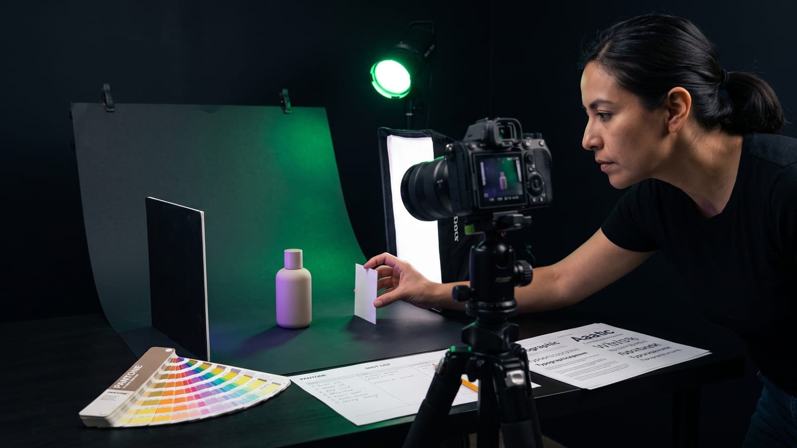 Fotógrafa tras una cámara réflex en tripié capta una botella cosmética en un mini set con softbox y shot list a mano: cuánto cuesta la fotografía de producto en México