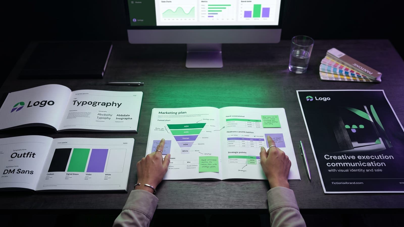 Mesa con tres estaciones: manuales de marca, plan de marketing con embudo AIDA y póster publicitario, contrastando branding, marketing y publicidad