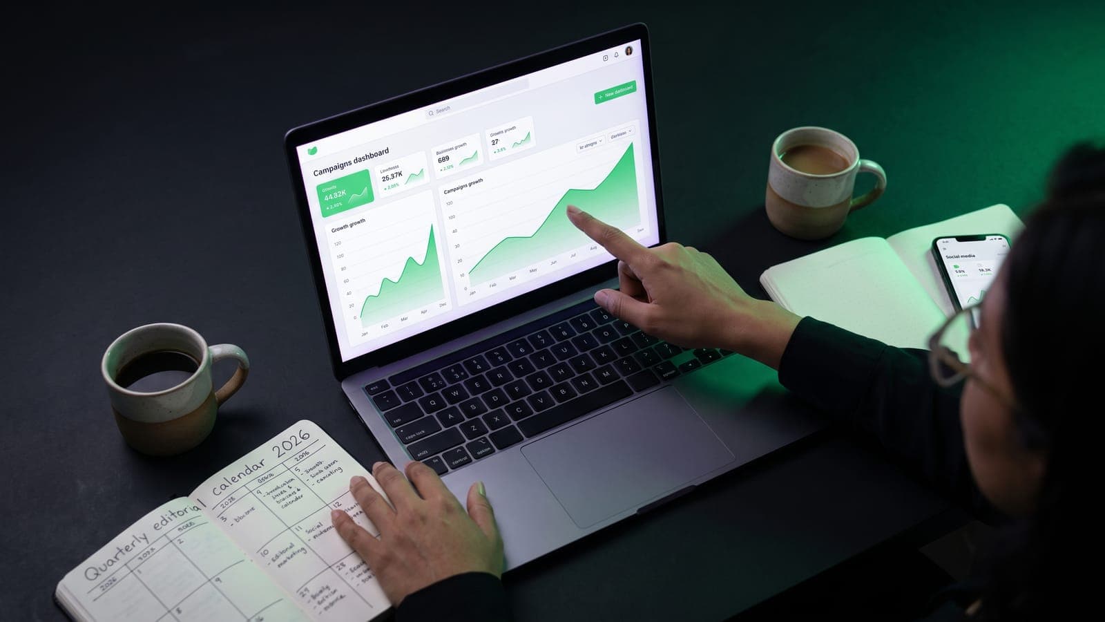 Estratega apuntando al dashboard de campañas en su laptop junto a un calendario editorial 2026 escrito a mano: marketing digital para PyMEs mexicanas