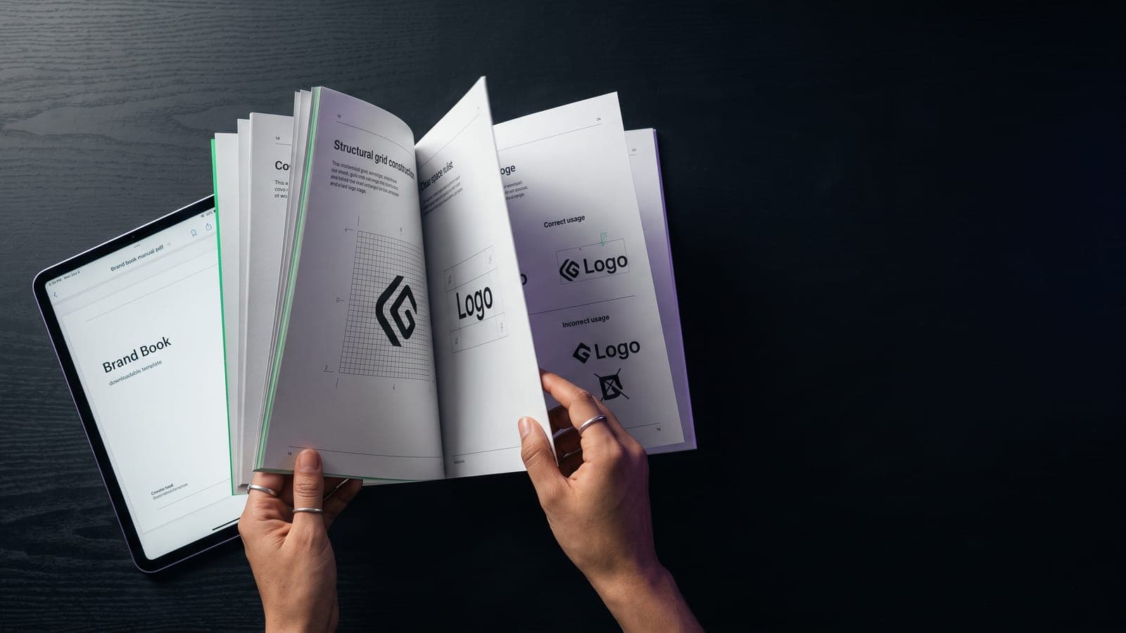 Manos hojeando un manual de marca impreso con retícula de construcción y usos correctos del logo, junto a una tablet con la plantilla PDF descargable