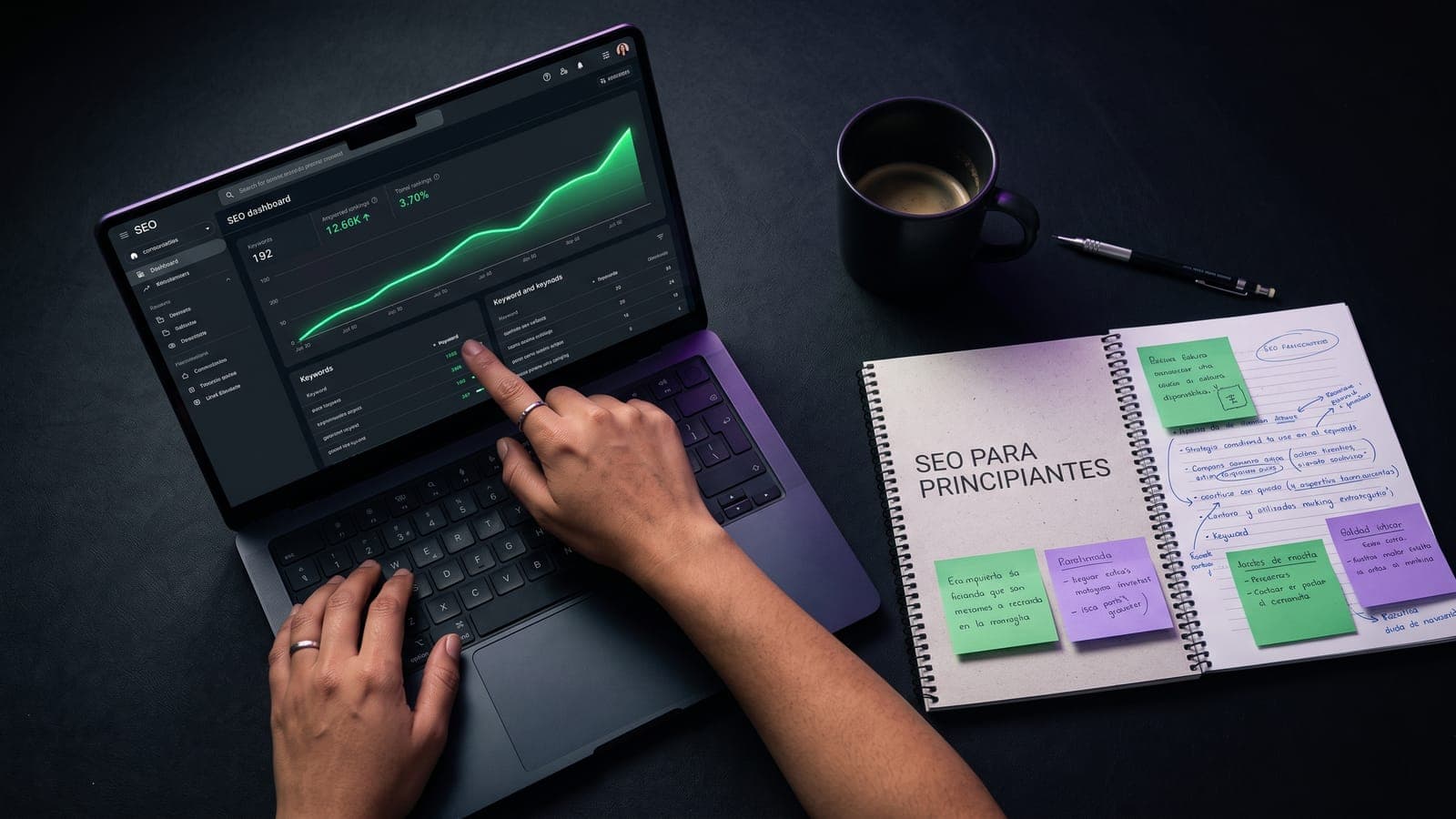 Laptop con dashboard SEO de posiciones y keywords junto a un cuaderno titulado SEO para principiantes con post-its de apuntes