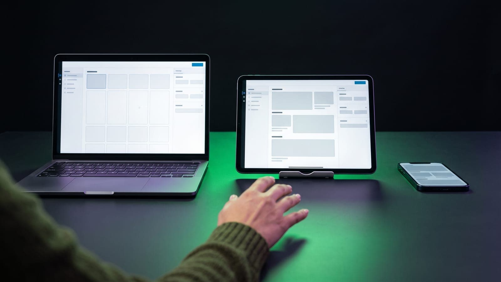 Laptop, tablet y smartphone alineados mostrando la interfaz de un constructor de sitios web sobre un escritorio con resplandor verde, al comparar Wix vs WordPress vs Squarespace
